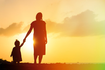 mother and little daughter walking on beach at sunset