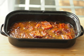 Baked pork belly with a sauce in a black roasting pan on a wooden table. Traditional specialty form...