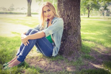 Full length portrait of smiling woman sitting under tree 