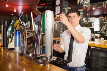 Bartender holding glass standing in front of beer dispenser