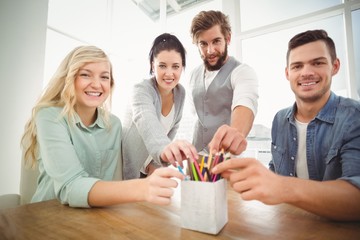 Portrait of smiling business people taking pencils 