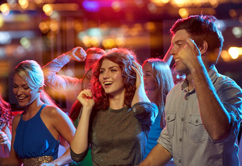 group of happy friends dancing in night club