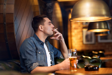 man drinking beer and smoking cigarette at bar