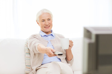 senior woman watching tv and drinking tea at home