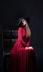 Woman in red evening dress sitting on a chair, dark background