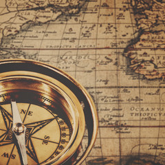 Retro brass compass over antique paper map, adventure background