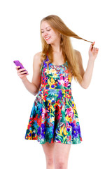Smile young teenager blonde girl in mix color dress sending a sms on cell mobile phone, isolated on white background