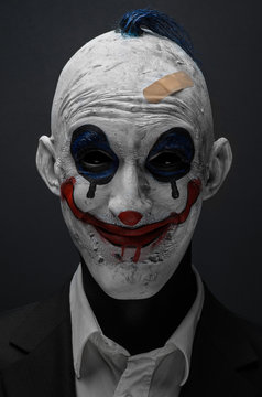 Terrible clown and Halloween theme: Crazy terrible blue clown in black suit isolated on a dark background in the studio