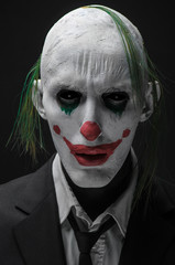 Terrible clown and Halloween theme: Crazy terrible green clown in black suit isolated on a dark background in the studio