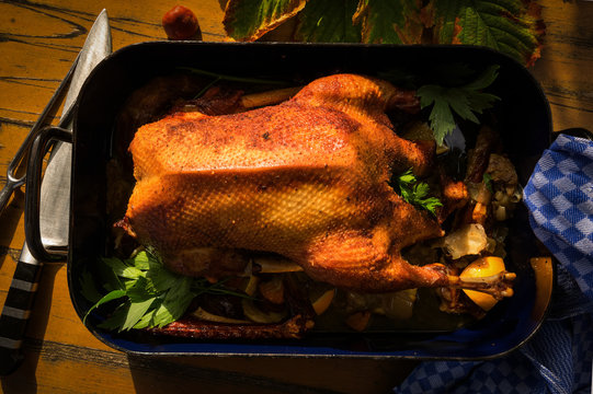 Ein knuspriger G&auml;nsebraten auf einem festlich gedeckten Tisch, umgeben von rustikalen Beilagen wie Rotkohl, Kartoffeln und Kr&auml;utern, in einer gem&uuml;tlichen, traditionellen Atmosph&auml;re."