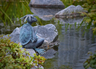 Бронзовая скульптура каппы сидящая на камне у пруда.