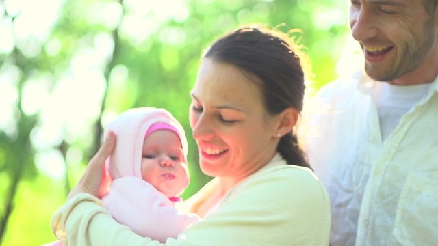 Happy family with little baby outdoors. Mother, father kissing newborn baby.