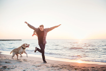 young caucasian male playing with labrador on beach during sunri