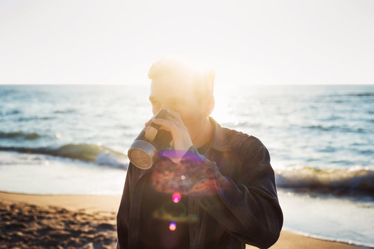 young caucasian male drinking coffee on beach while walking with
