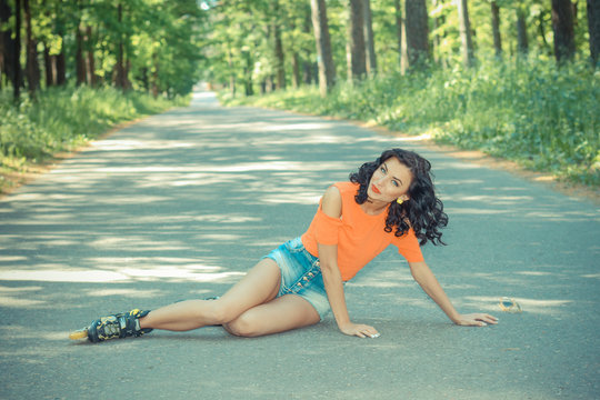 Portrait of positive crazy cheerful girl on roller skates. Young woman in roller skates, sitting on the road looking at camera and smiling. happy young brunette woman on roller skates in the park
