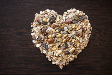 Heart-shaped muesli and cereal on dark wooden background