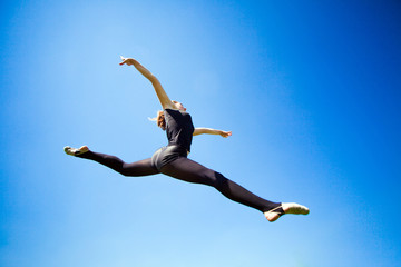 Fototapeta premium Smiling young gymnast is jumping in split and floating above the