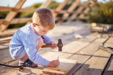 Child (boy) hammers nails with a hammer  in a wooden board on the roof