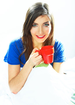 Woman sitting in bed with red coffee cup.