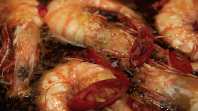 Close up pan of whole shrimps sizzling in a chili marinade in a fry pan.