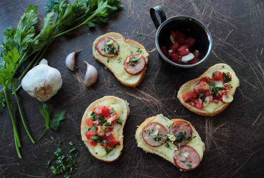 Bruschettas on wooden table with tomatoes, cheese, sausage, garlic and fresh herbs
