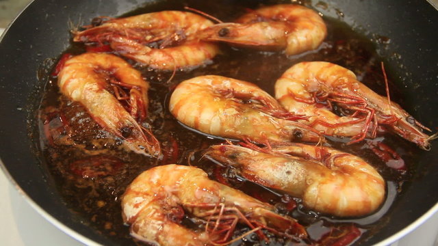 Whole shrimps sizzling in a chili marinade being turned with tongs in a fry pan.