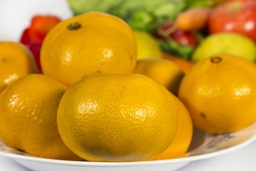 Close-up of orange tangerines into a dish, in front of several vegetables