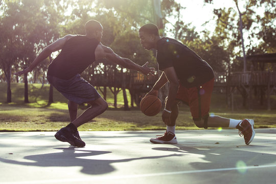 Two young men playing basketball in the park at sunset