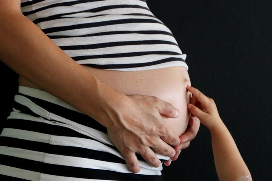Pregnant woman holding her belly and her baby girl touching her navel