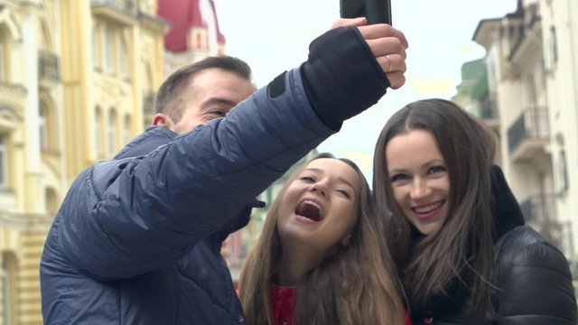 Young happy family and teen daughter doing selfie on smartphon outdoor