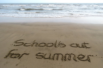 Schools out for summer written in sand, with the sea in the background
