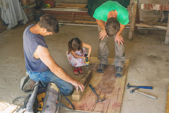 Girl helping two workmen drill a hole in a piece of  wood