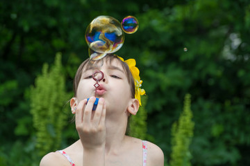 Little girl inflates soap bubbles in the garden