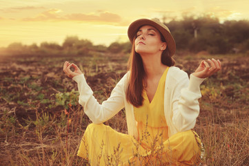 Female meditate sitting on a deadwood autumn field.