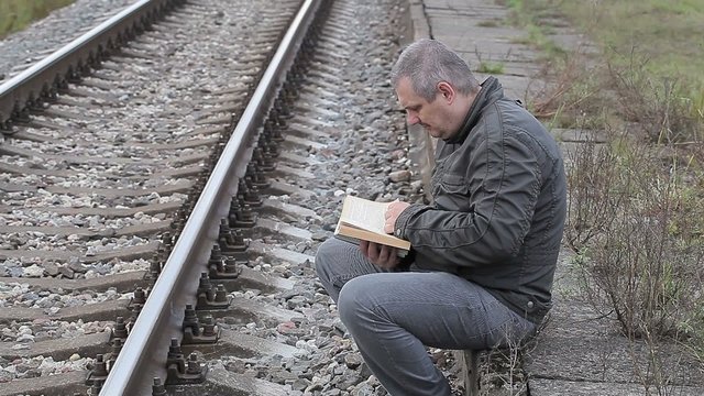 Man reading book near railway at outdoor