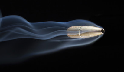 Speeding bullet with smoke behind after a shooting on a black background © Guy Sagi
