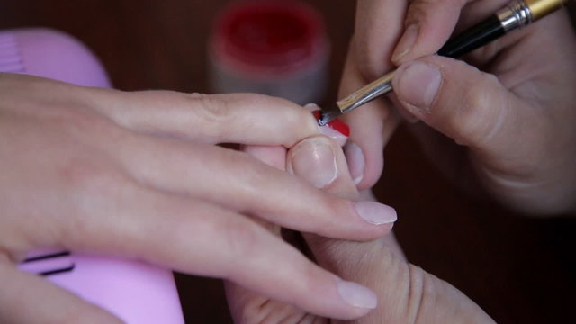 master applying red nail polish on klient fingers