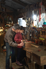 Portrait of a middle age gray hair man with beard working with his little girl in the workshop. They are focused while hammering a nail on a wooden birdhouse. They are wearing jeans and woolen pulls.