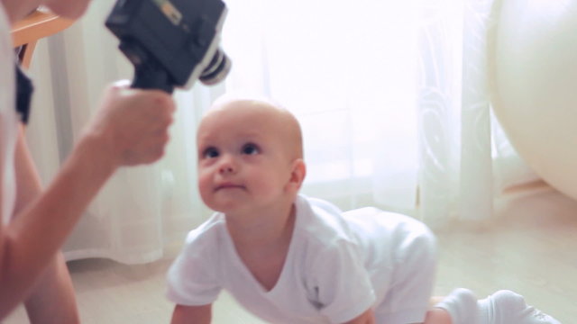 Mother making movie of her baby boy using retro movie camera in sunny living room