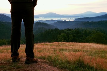 Woman hiker legs in tourist boots stand on hill  peak, dry grass in meadow