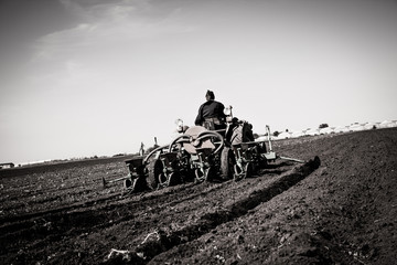 Farmer in Old-fashioned tractor sowing crops at field, Black and white