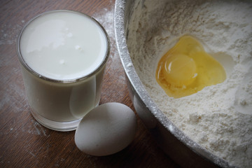 Still life. Flour with an egg in a bowl and glass of milk on the table. 