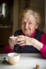 Portrait of an old woman drinking tea at a table in the kitchen.