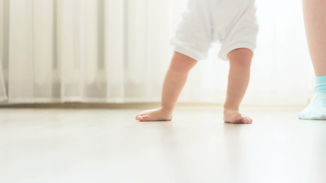 Close-up of baby boy walking his first steps with his mother support 