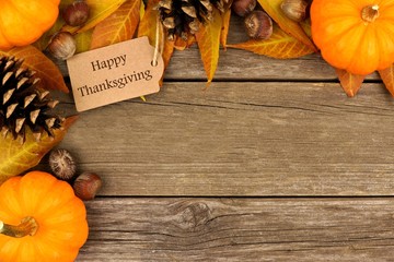 Happy Thanksgiving gift tag with corner border of colorful leaves and pumpkins over a rustic wood background