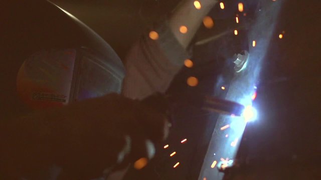 Worker welding metal by electrode with bright electric arc