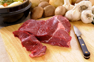 Preparing beef steak for casserole or stew with crockpot vegetable ingredients chopping board and knife photo