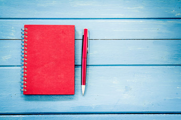 Red notebook with pen on blue wooden table