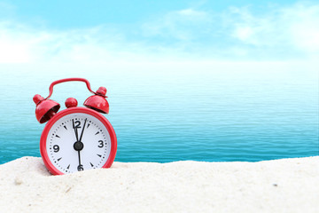 small clock on white sea sand and blur ocean background