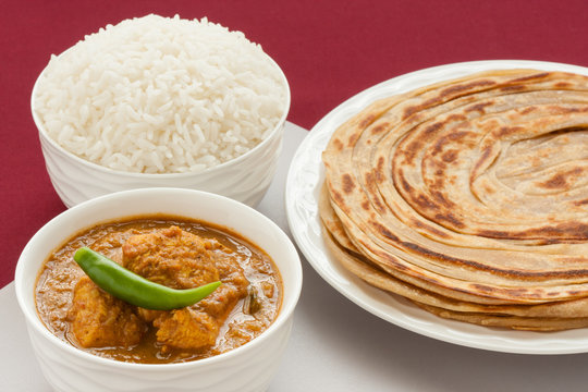 Indian chicken curry meal - Closeup view of Indian chicken curry meal with rice and wheat parotta (Indian bread). Green chilli used as garnish. Natural light used.